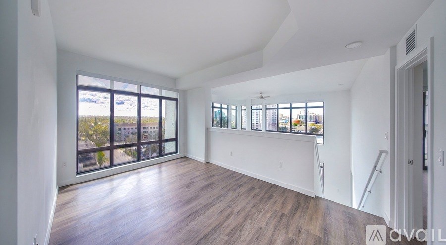 A spacious room with wooden floors and large windows overlooking a cityscape.