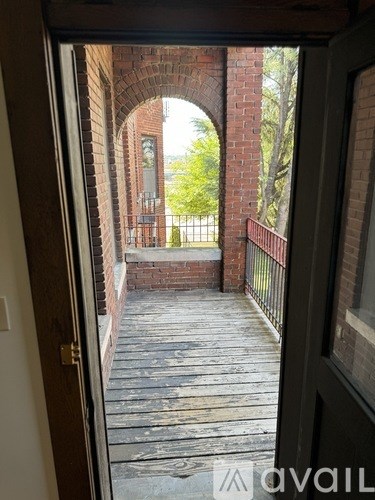 A view from inside a building looking out through an arched doorway to a brick building and a metal fence.