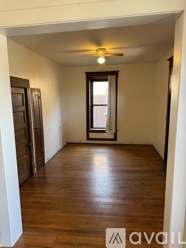 A room with wooden floors and a window with a view of a brick building.