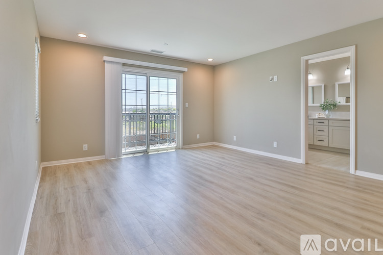 A spacious room with wooden flooring and a large window with a view of a fence and trees.