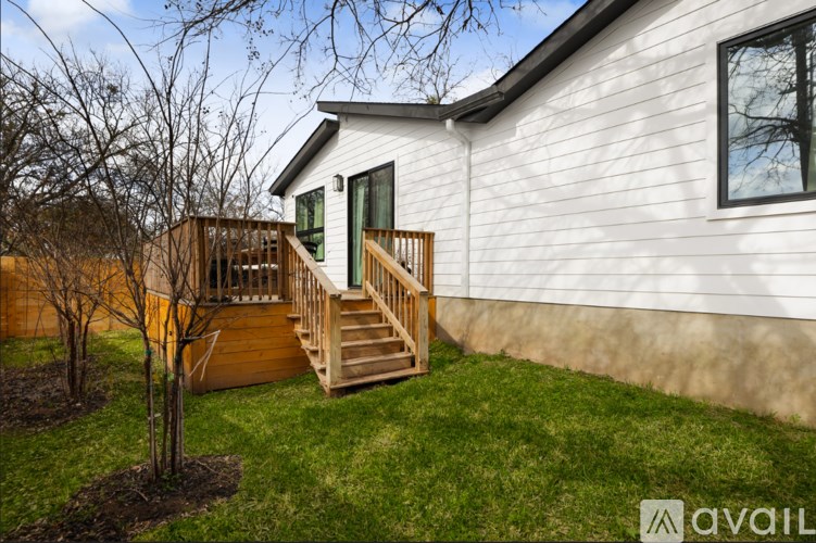 A house with a white exterior and a deck with stairs leading to a green door.