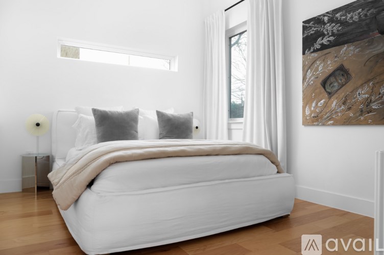 A white bed with a beige blanket and two grey pillows in a room with a large painting on the wall.