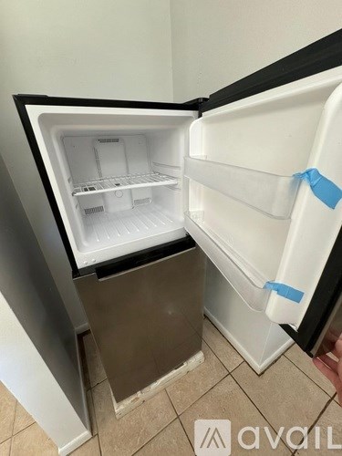 A white refrigerator with its door open and a blue tape on the door.