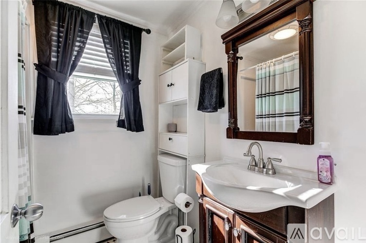 A bathroom with a white toilet, a sink with a mirror above it, and a window with black curtains.