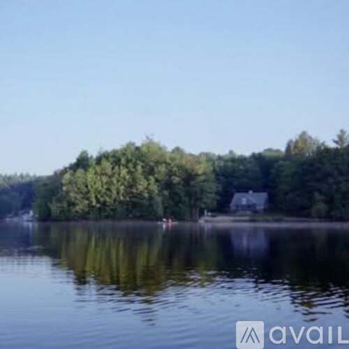 A serene lake with a house and trees in the background.