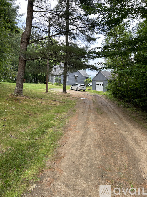 A dirt road leads to a house with a car parked in front.