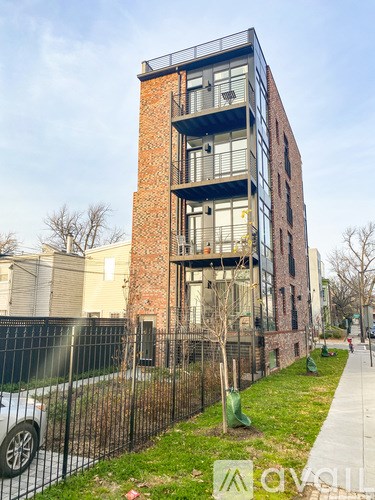 A modern brick building with balconies and a black fence in front.