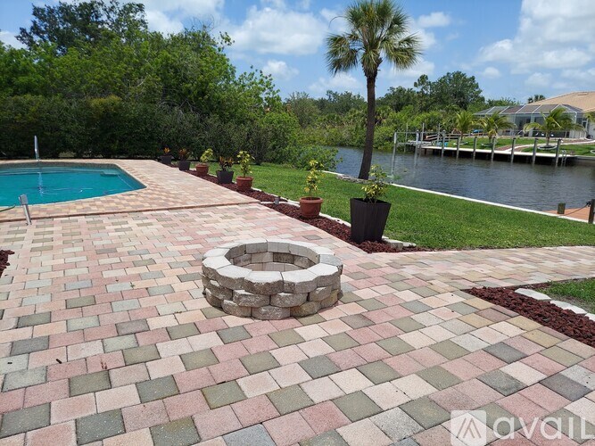 A brick patio with a fire pit and a pool in the background.