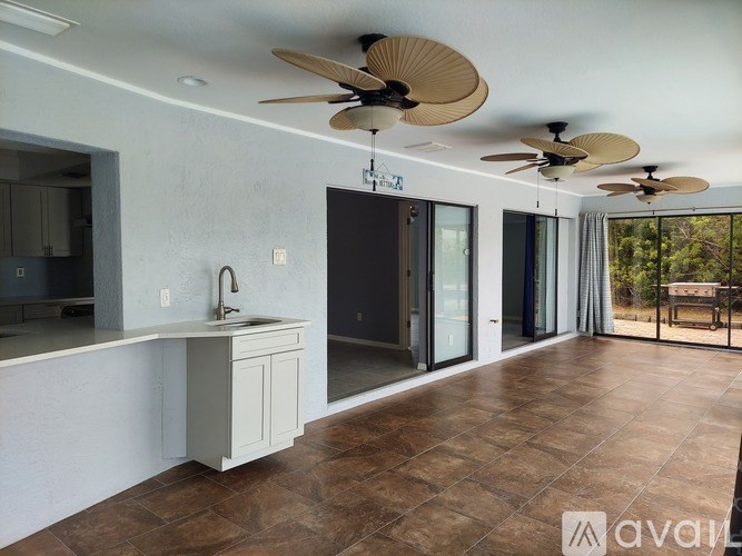 A kitchen with a white countertop and a sink, a fan, and a sliding glass door.