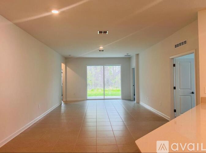 A spacious room with tiled flooring and a sliding glass door leading to a garden.