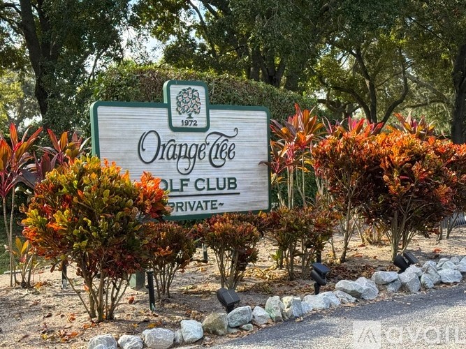 A sign for the Orange Tree Golf Club stands in front of some shrubbery.