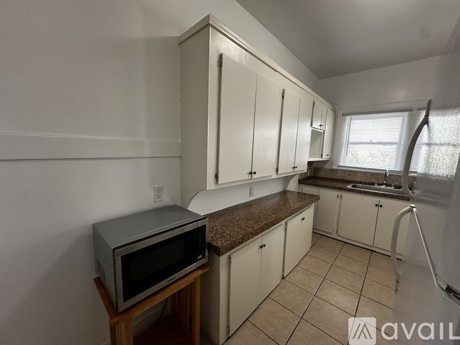 A kitchen with white cabinets and a microwave on a wooden stand.
