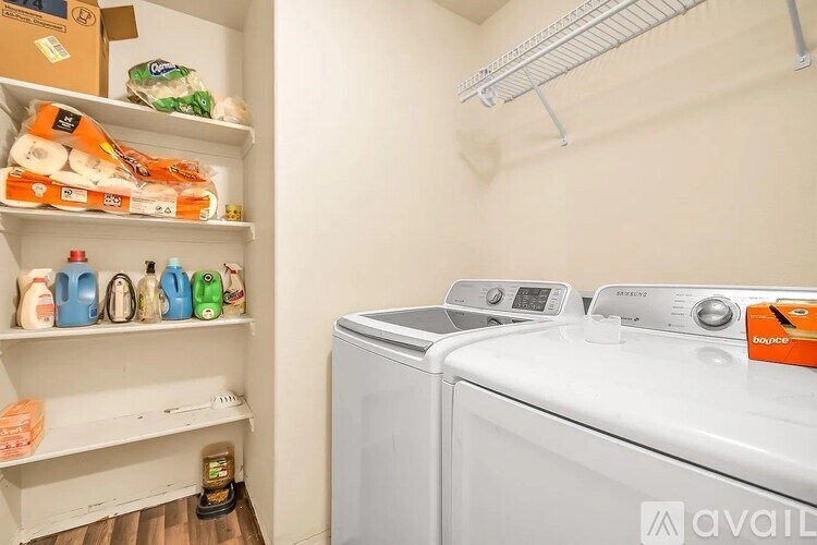 A laundry room with a washer and dryer and a shelf with toilet paper and detergent.