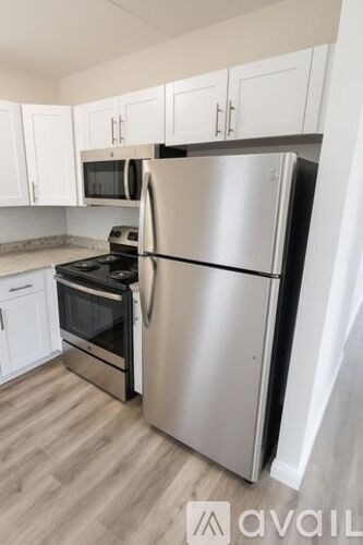 A stainless steel refrigerator stands in a kitchen with white cabinets.