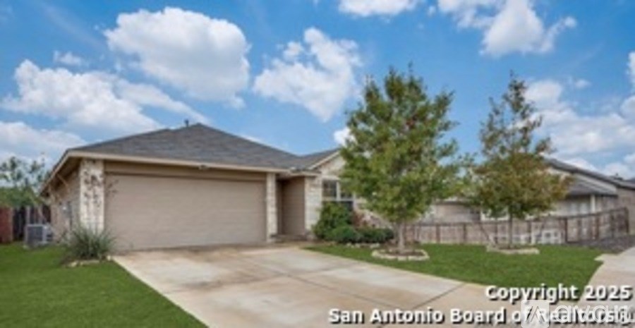 A house with a brown roof and a garage door is surrounded by a fence and trees.