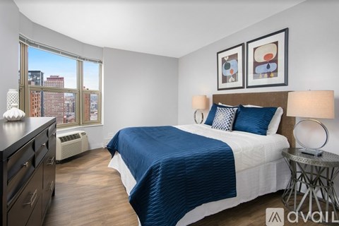 A bedroom with a large bed and a city view through the window.
