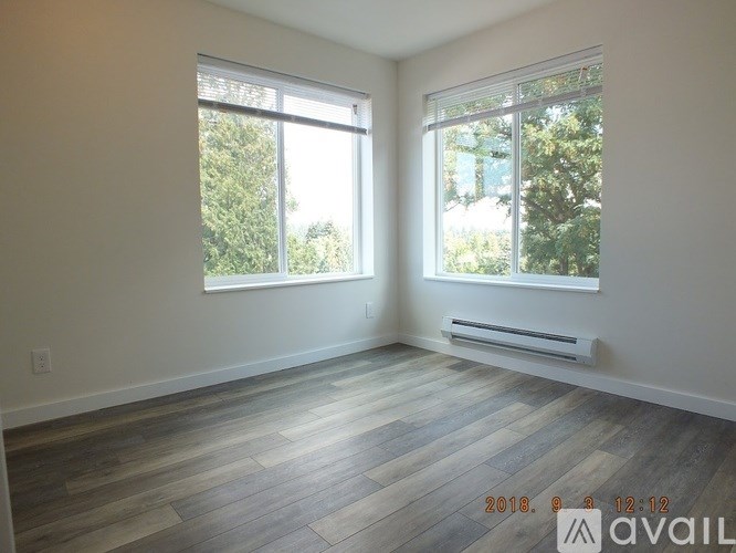 A room with wooden flooring and two windows overlooking trees.