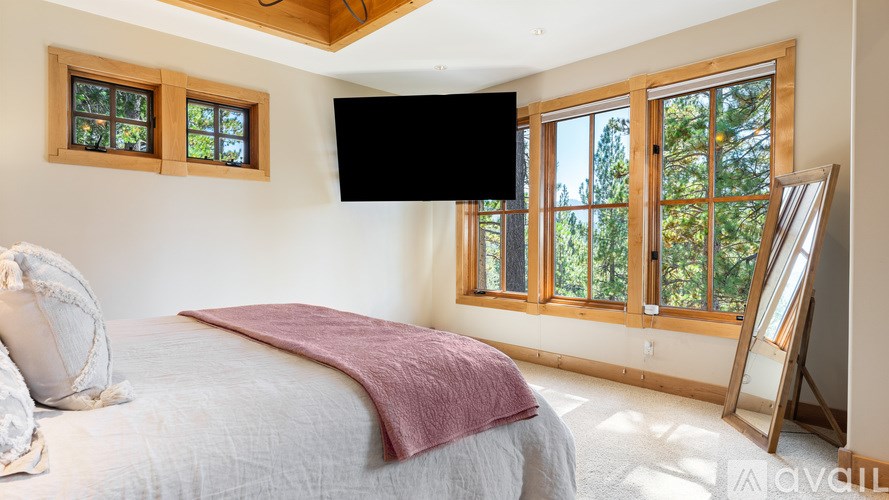 A bedroom with a bed, a window, and a flat screen TV mounted on the wall.