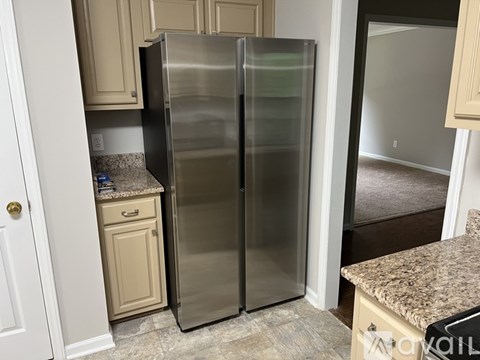 A stainless steel refrigerator stands in a kitchen with beige cabinets.