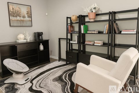 A living room with a white chair, a black bookshelf, and a rug with a black and white pattern.