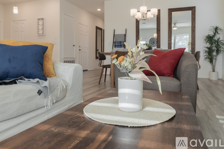 A living room with a white sofa, a grey armchair, a wooden coffee table, and a white vase with flowers on a round rug.