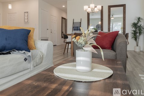 A living room with a white sofa, a grey armchair, a wooden coffee table, and a white vase with flowers on a round rug.