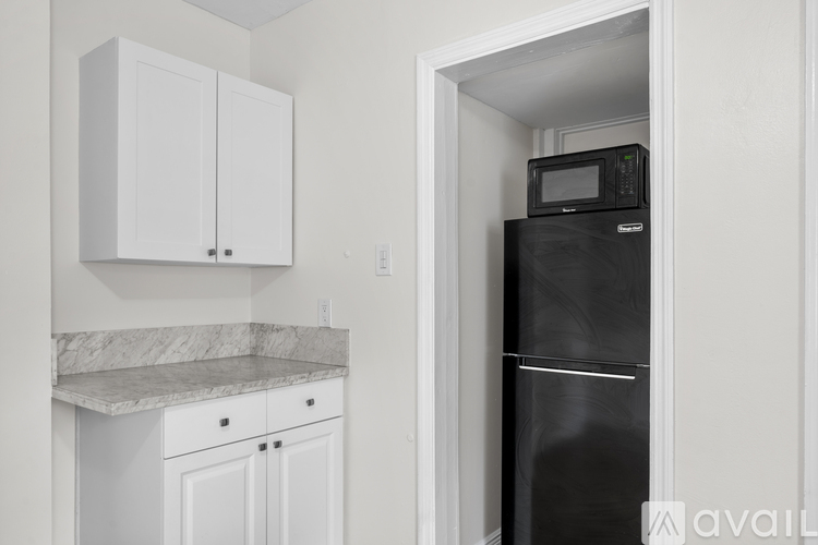 A black refrigerator is in a kitchen with white cabinets.