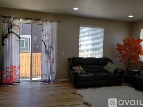 A living room with a black couch and a tree with orange leaves.