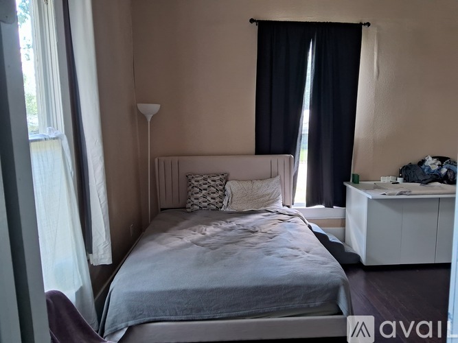 A bedroom with a bed, nightstand, and window with curtains.
