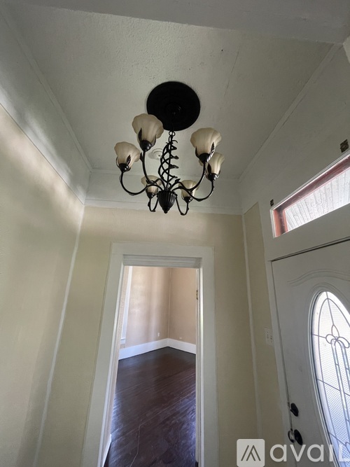 A chandelier hangs from the ceiling in a room with white walls and wood flooring.