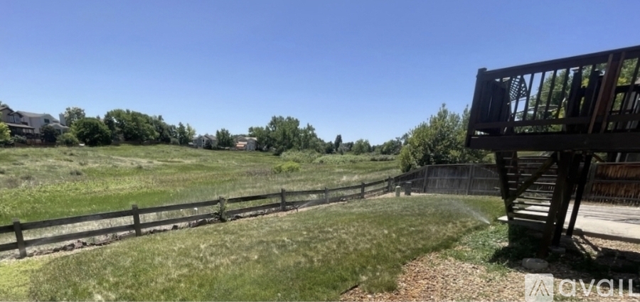 A wooden deck overlooks a grassy field with a fence.