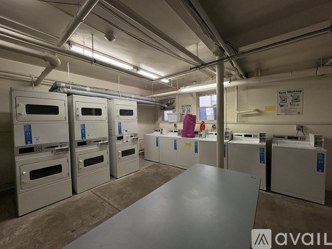 A room with a table in the foreground and several ovens in the background.