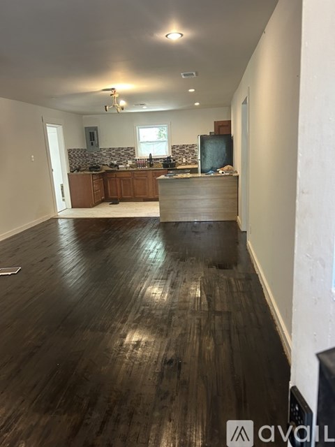 A spacious room with wooden floors and a kitchen area in the background.