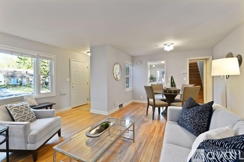 A living room with a grey couch, a glass coffee table, and a dining table with chairs.