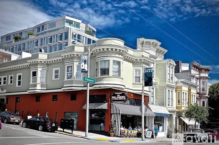 A street view of a city with cars parked and buildings with a cafe in the middle.
