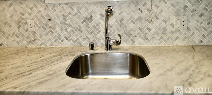 A stainless steel sink in a marble countertop with a chrome faucet.