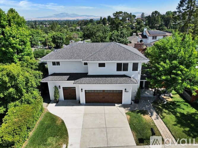A large white house with a brown garage door is surrounded by greenery.