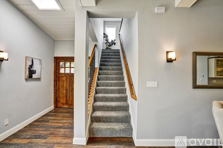 A staircase with a wooden handrail and a carpeted runner leads up to a landing with a mirror and a door.