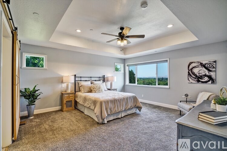 A bedroom with a large bed, a ceiling fan, and a window overlooking a landscape.