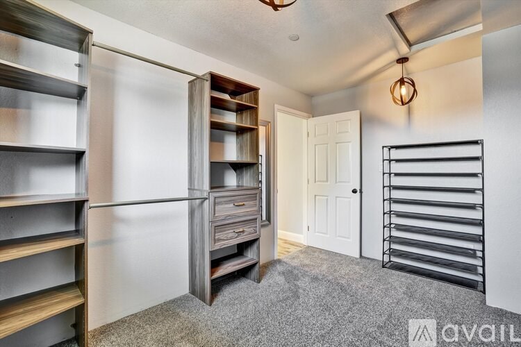 A room with a white door, a grey carpet, and a wooden shelf unit.