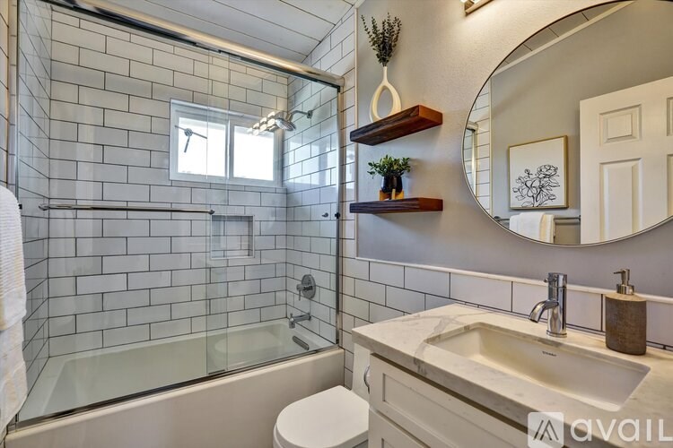 A bathroom with a glass shower stall, a white toilet, a sink, and a mirror.