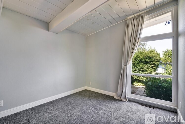 A room with a window and a grey carpet.