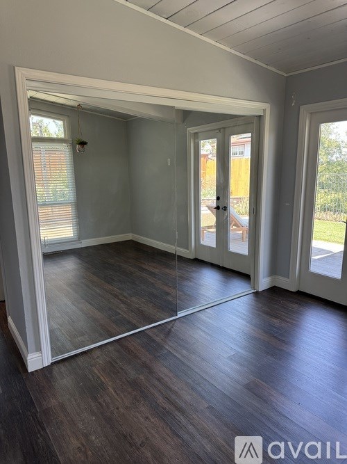 A spacious room with wooden floors and white walls, featuring a large open doorway leading to a balcony.