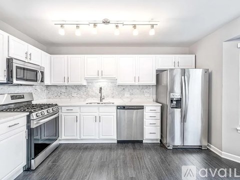A kitchen with white cabinets and appliances, a stove, a sink, and a refrigerator.