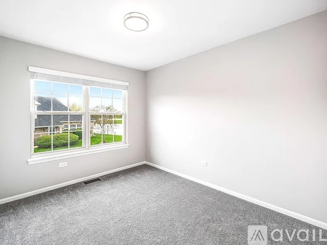 A room with a window showing a view of a house and trees outside.