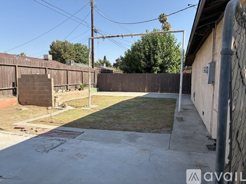 A backyard with a fence, a small patch of grass, and a concrete slab with a logo on it.