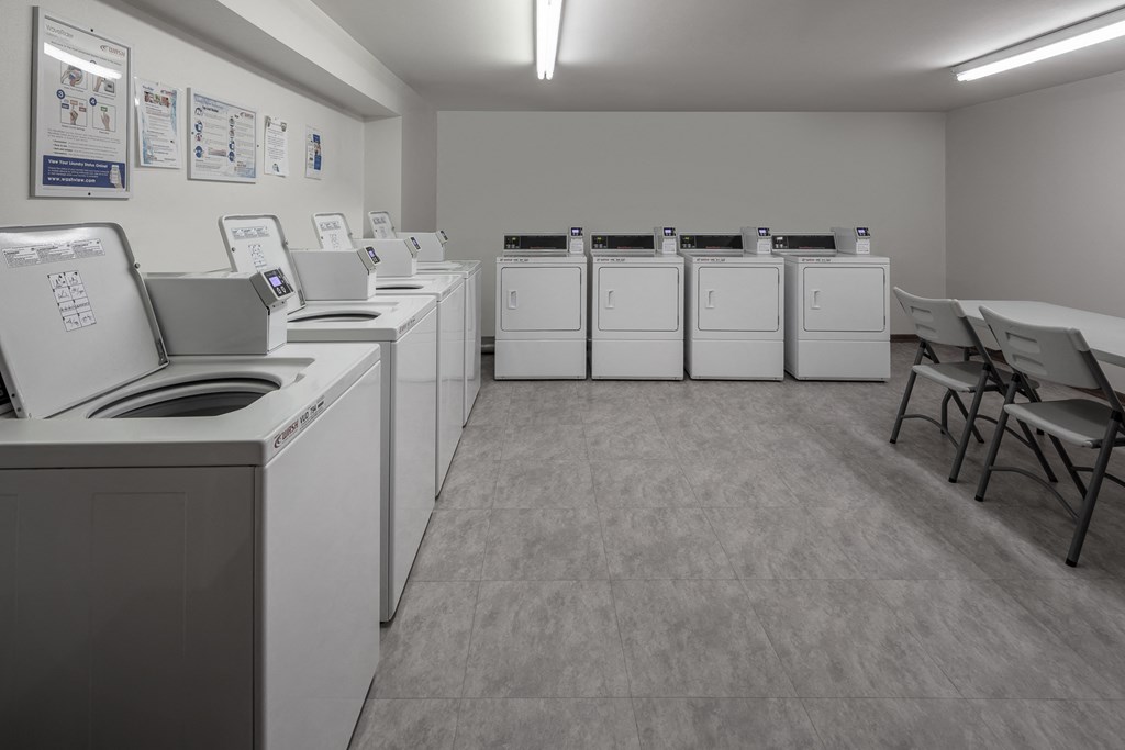 a row of washers and dryers in a laundry room with tables and chairs
