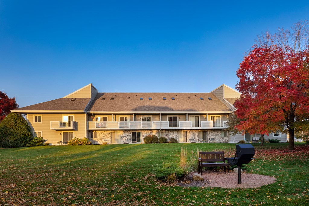 a large yellow apartment building with a park bench and a grill