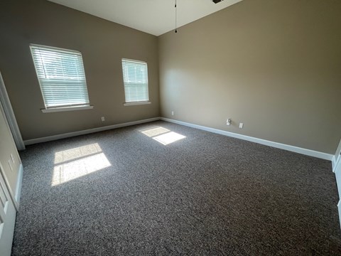 A room with grey carpet and two windows letting in sunlight.