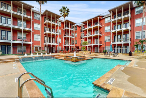 A large red apartment complex with a pool in the middle.